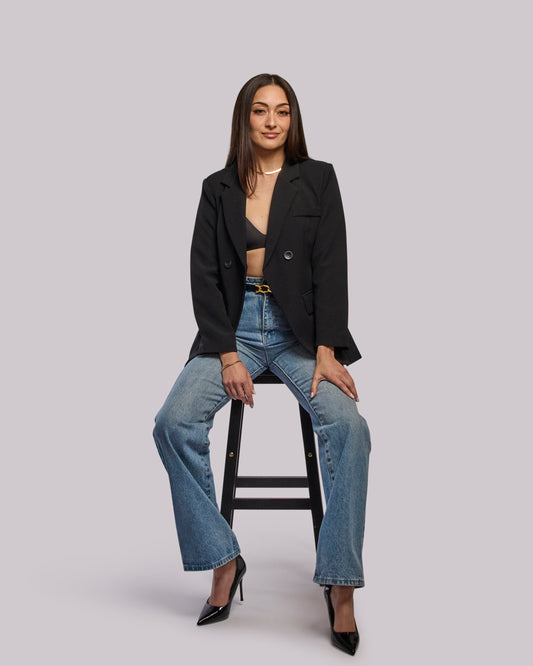 Model wearing Roar blazer open from front and sitting on stool