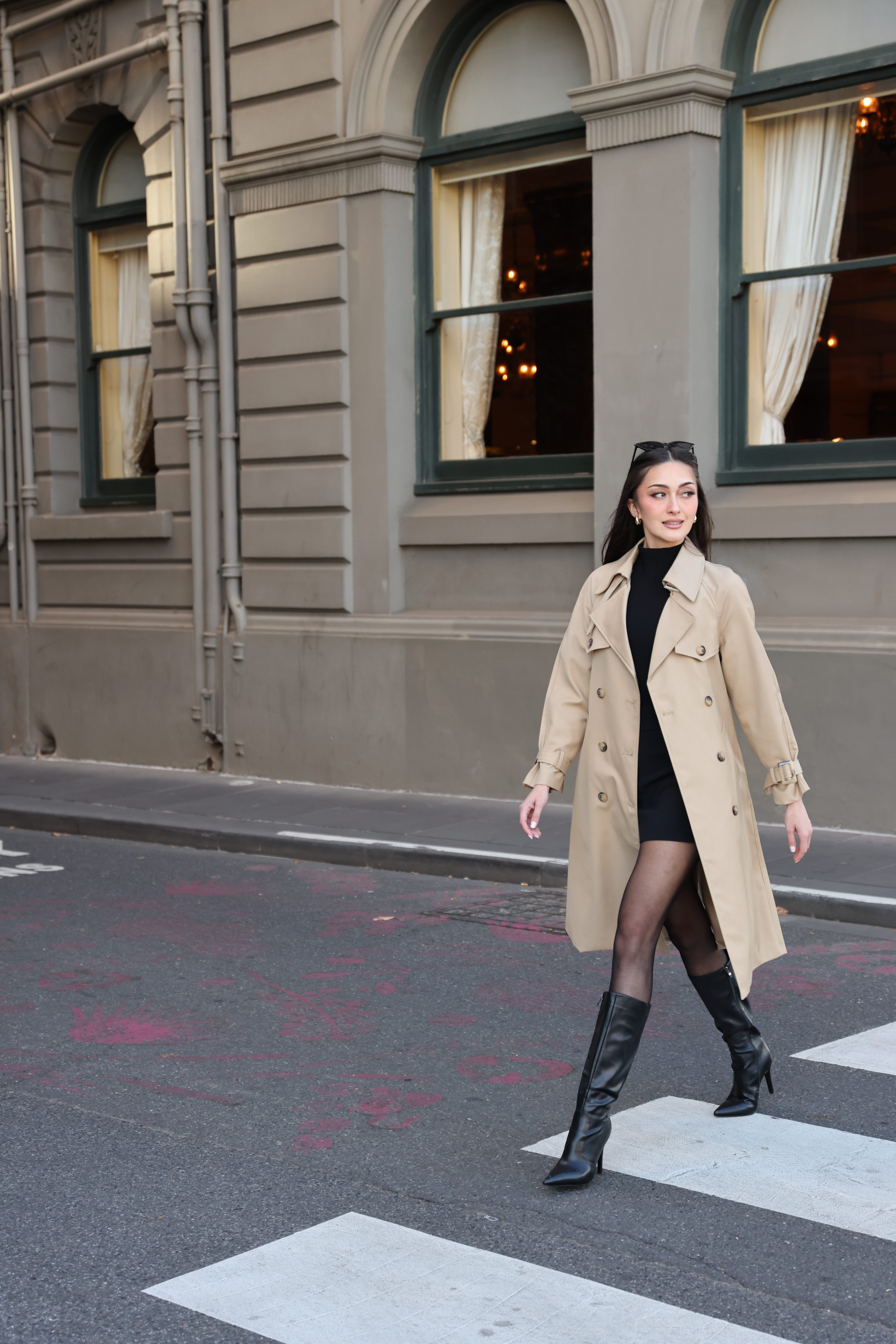 Woman in a beige trench coat walking on a city street.