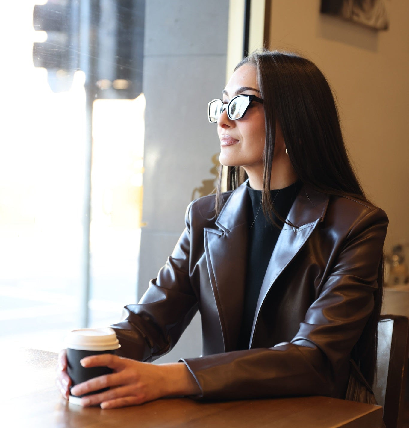Woman sitting at a table in a cafe, holding a coffee cup.