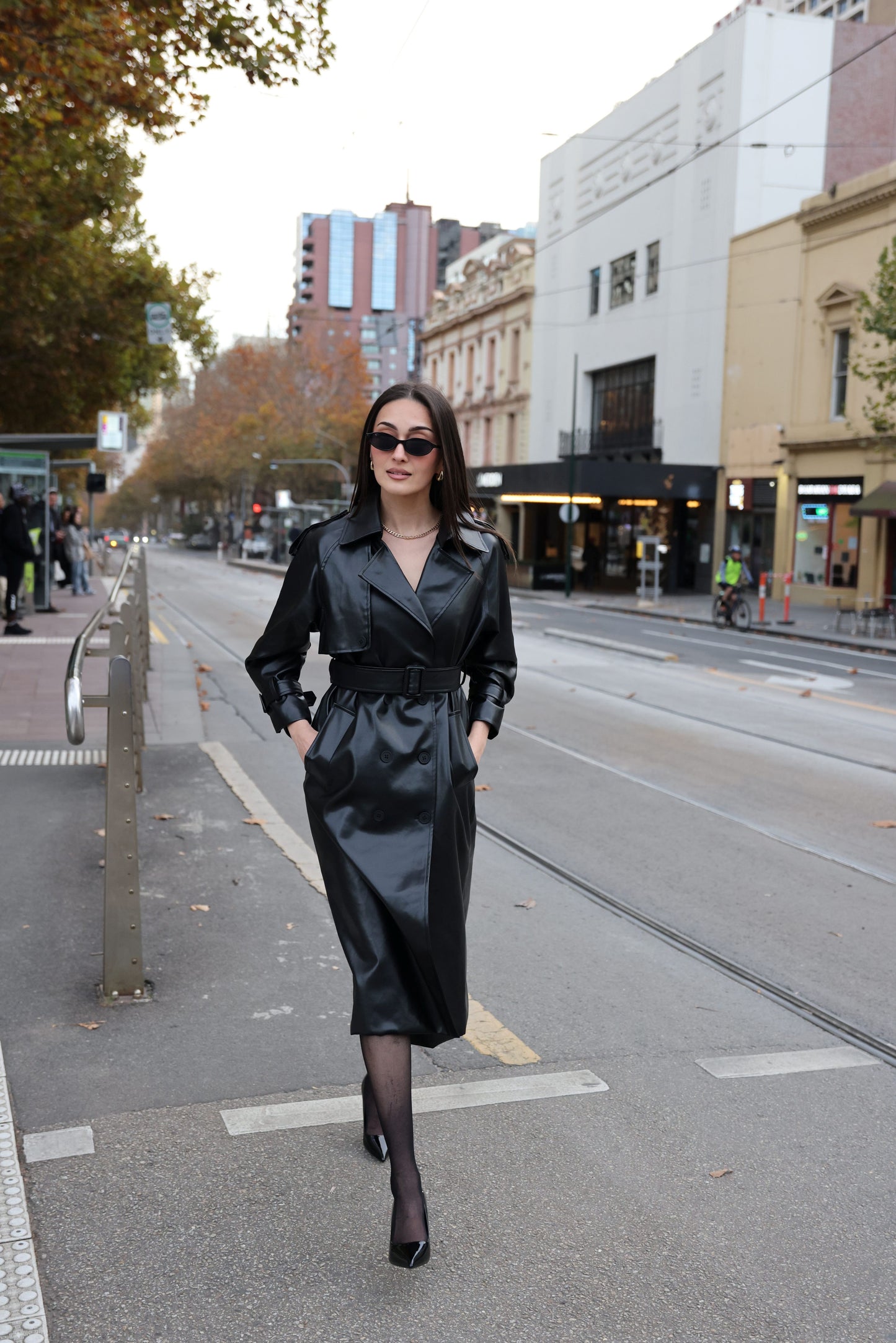 Woman in a black leather coat walking on a city street.